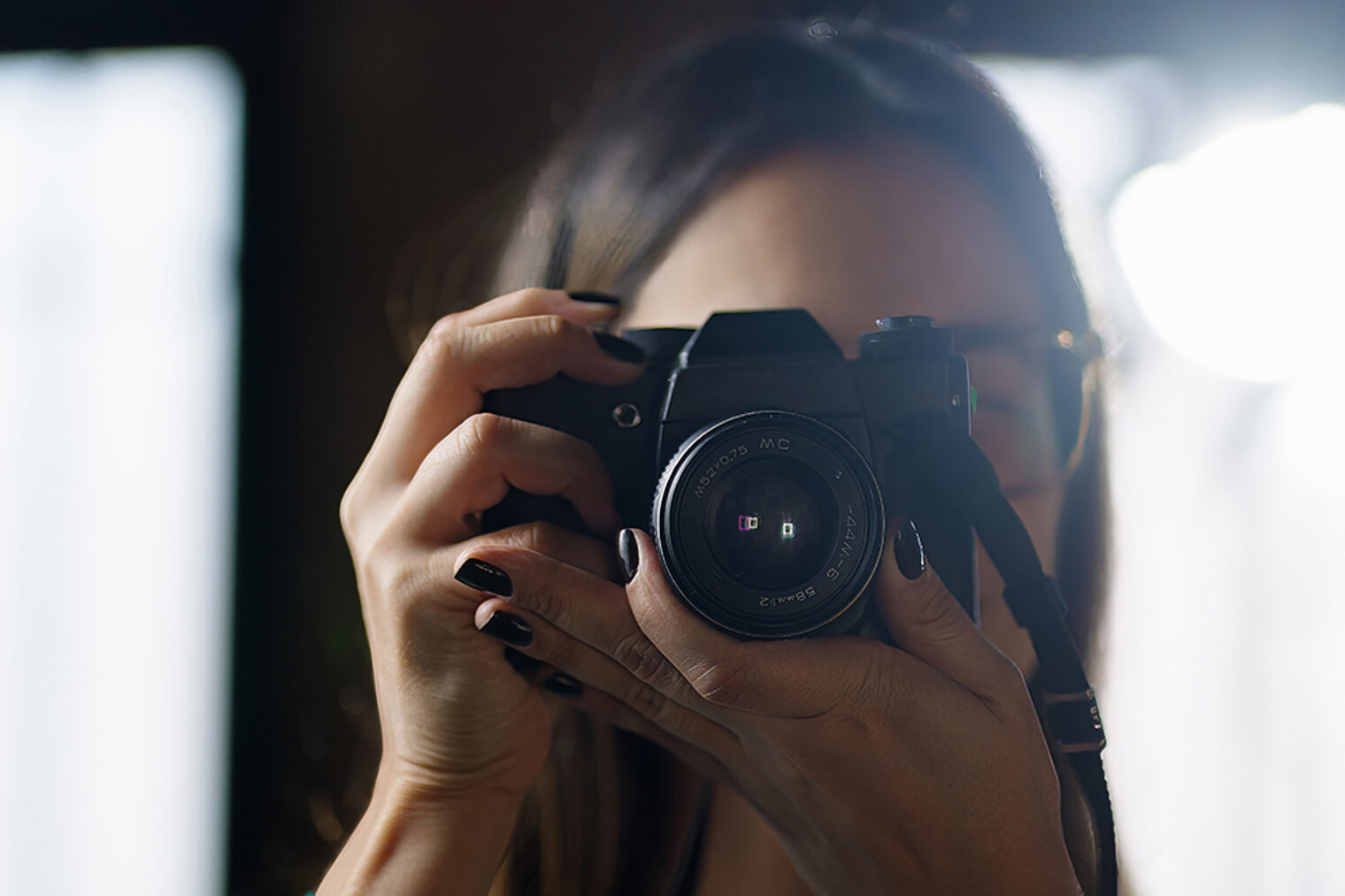 Fotografin im Fokus: Kamera vor dem Gesicht im natürlichen Licht Frau mit dunklem Nagellack fotografiert mit Spiegelreflexkamera im Gegenlicht