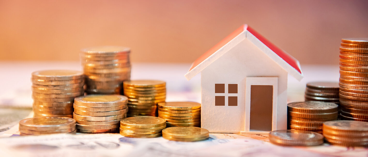 Hausfinanzierung, Investition oder Vermögensaufbau im Fokus Symbolisches Hausmodell zwischen Münzstapeln auf Geldscheinen, Fokus auf Baufinanzierung oder Investitionen