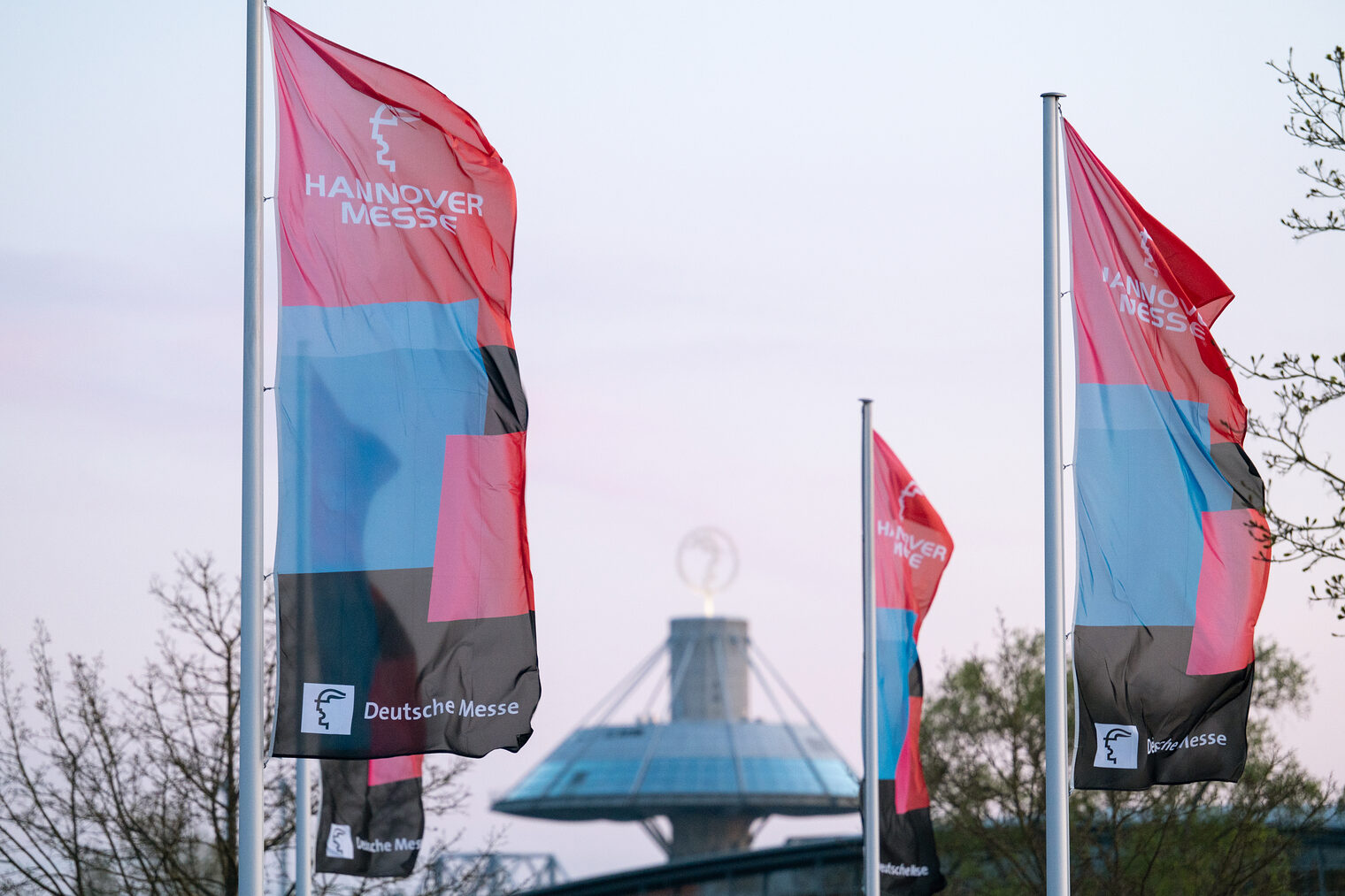 HANNOVER MESSE-Fahnen auf dem Messegelände mit Expo-Dach im Hintergrund bei Abendlicht